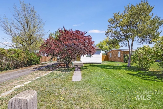 view of property hidden behind natural elements with fence and a front lawn