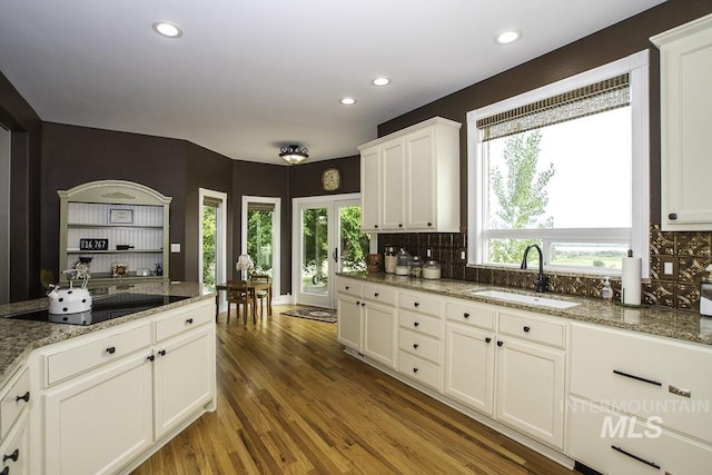 kitchen featuring recessed lighting, backsplash, black electric cooktop, a sink, and wood finished floors
