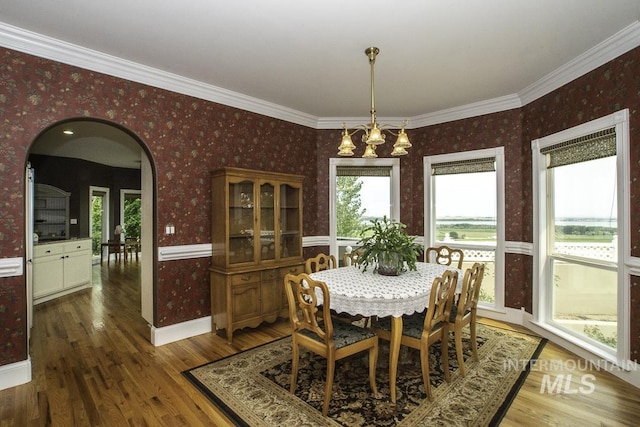 dining area featuring arched walkways, wallpapered walls, and wood finished floors