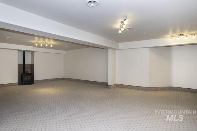 finished basement with visible vents, a wood stove, carpet, and track lighting