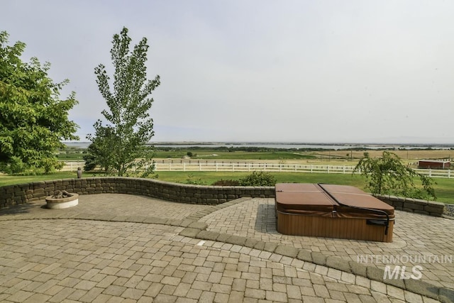 view of patio / terrace featuring a rural view, a covered hot tub, and fence