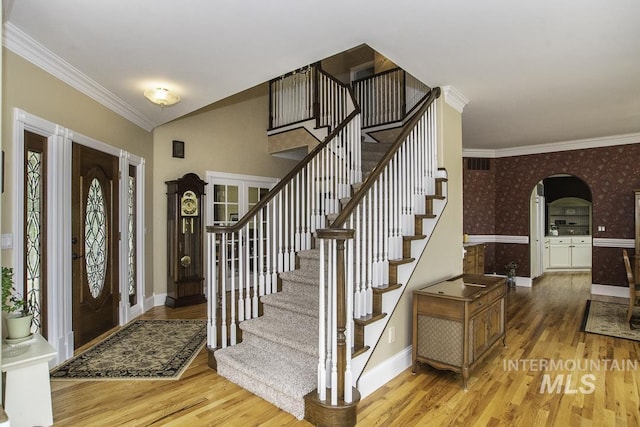 foyer with crown molding, light wood-style flooring, arched walkways, and wallpapered walls