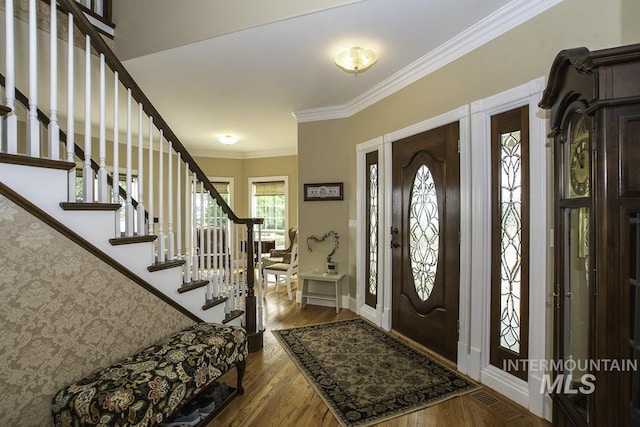 foyer entrance with wood finished floors, baseboards, ornamental molding, and stairway