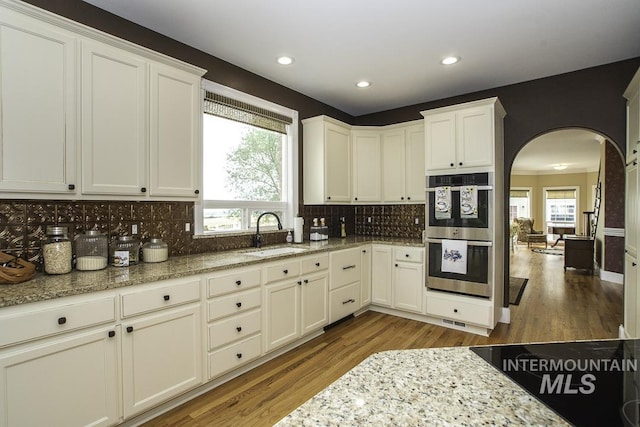 kitchen featuring decorative backsplash, wood finished floors, stainless steel double oven, and a sink