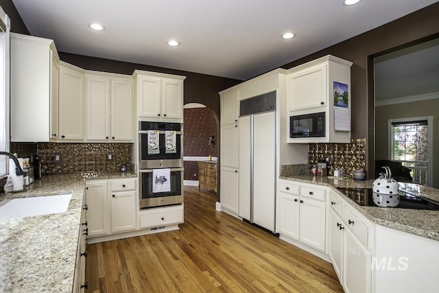 kitchen featuring light wood-style flooring, black appliances, decorative backsplash, arched walkways, and a sink