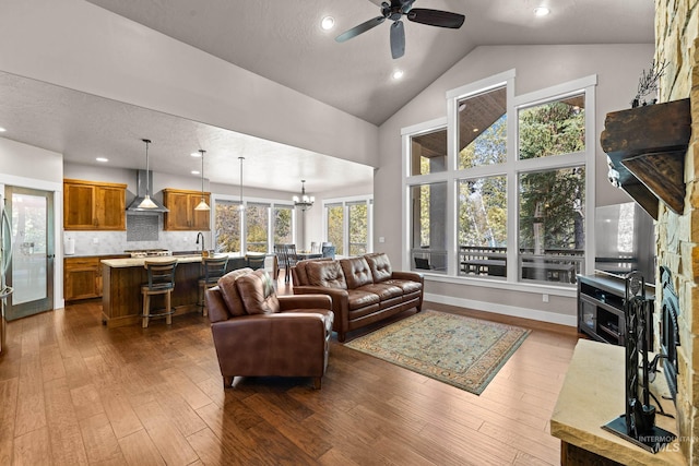 living room featuring ceiling fan with notable chandelier, a textured ceiling, a fireplace, and dark wood-type flooring