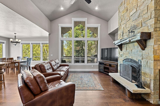 living room featuring ceiling fan with notable chandelier, dark hardwood / wood-style flooring, a textured ceiling, and a stone fireplace