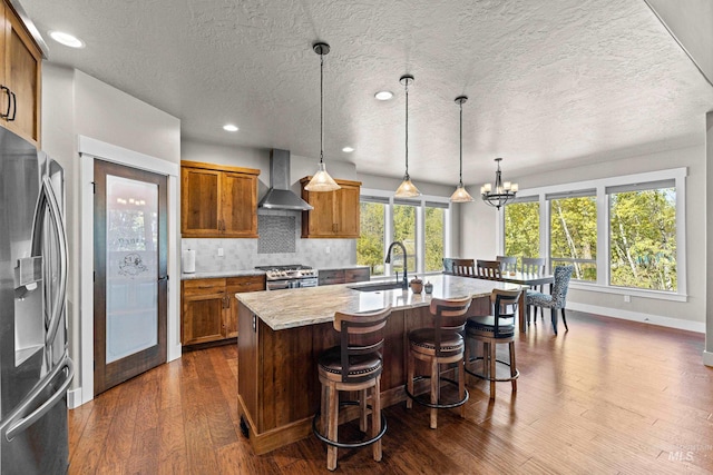 kitchen featuring appliances with stainless steel finishes, an island with sink, wall chimney exhaust hood, dark hardwood / wood-style floors, and sink