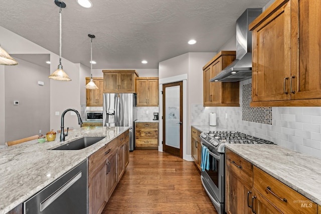 kitchen with pendant lighting, sink, wall chimney exhaust hood, appliances with stainless steel finishes, and dark hardwood / wood-style flooring