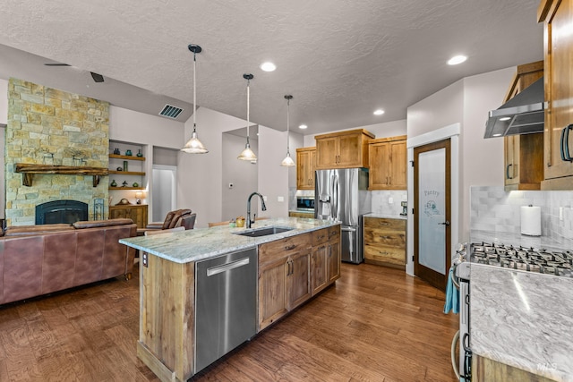 kitchen featuring appliances with stainless steel finishes, dark wood-type flooring, a fireplace, a kitchen island with sink, and sink