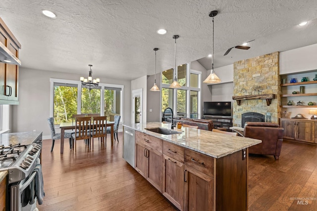 kitchen featuring appliances with stainless steel finishes, a fireplace, light stone countertops, a center island with sink, and sink