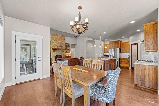 dining space featuring sink, a stone fireplace, a textured ceiling, light hardwood / wood-style flooring, and an inviting chandelier