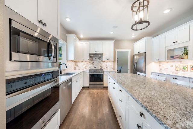 kitchen with light stone countertops, appliances with stainless steel finishes, white cabinets, a sink, and wood finished floors