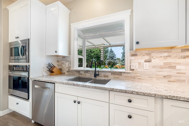 kitchen with appliances with stainless steel finishes, white cabinets, a sink, and backsplash