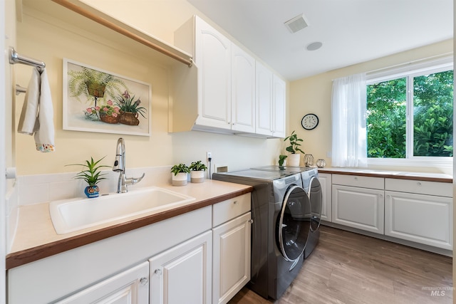 clothes washing area with wood finished floors, visible vents, a sink, independent washer and dryer, and cabinet space