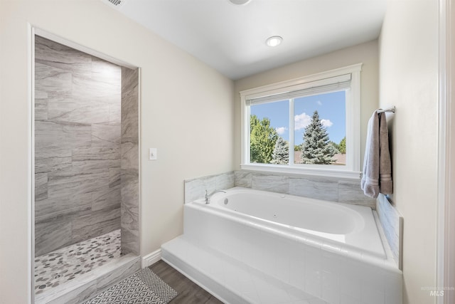 bathroom featuring a garden tub, a tile shower, baseboards, and wood finished floors