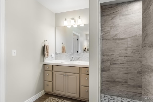 bathroom with wood finished floors, a tile shower, vanity, and baseboards