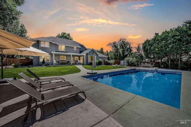 pool at dusk featuring a fenced backyard, a fenced in pool, a lawn, and a patio