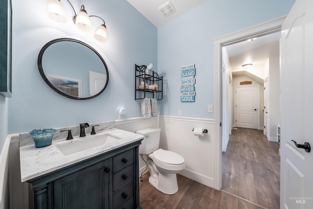 bathroom with toilet, wood finished floors, vanity, visible vents, and wainscoting