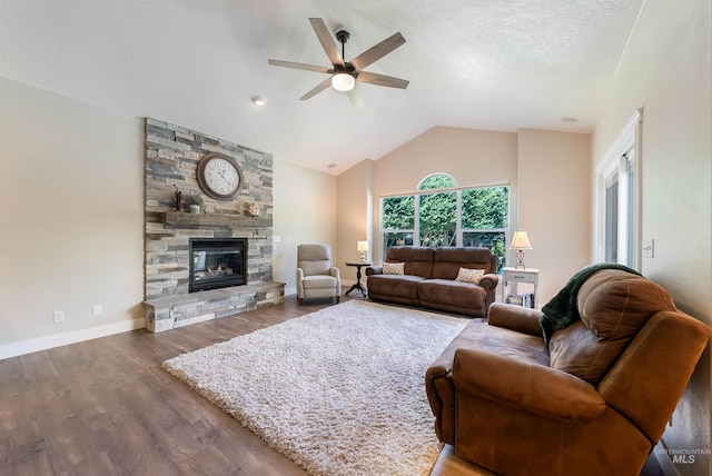 living area with a ceiling fan, vaulted ceiling, a stone fireplace, wood finished floors, and baseboards