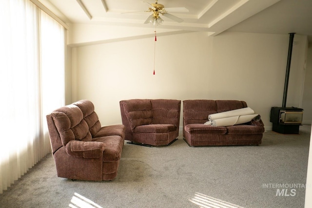 living room featuring ceiling fan, light carpet, a tray ceiling, and a wood stove