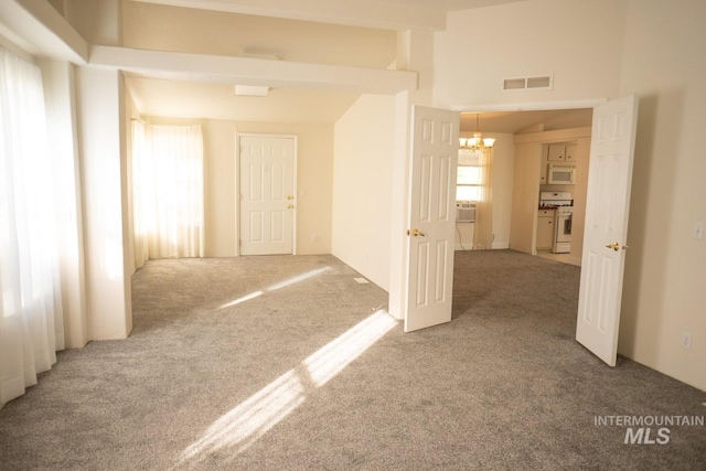 spare room featuring light colored carpet, a notable chandelier, a high ceiling, and beam ceiling