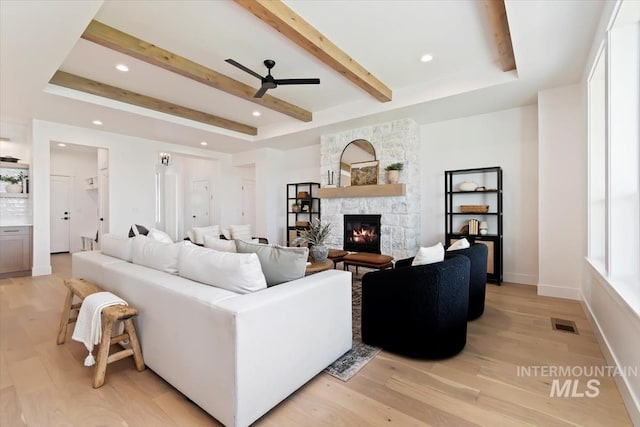 living area featuring light wood-type flooring, beam ceiling, visible vents, and a stone fireplace