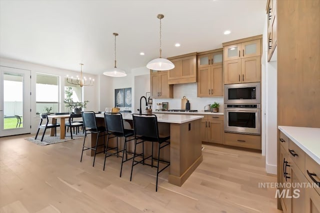 kitchen featuring an island with sink, a kitchen breakfast bar, stainless steel appliances, light countertops, and light wood-type flooring