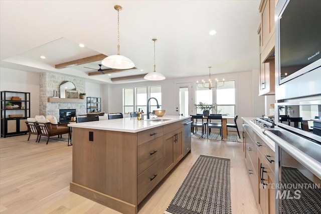 kitchen with stainless steel appliances, light countertops, a stone fireplace, light wood-style floors, and a sink