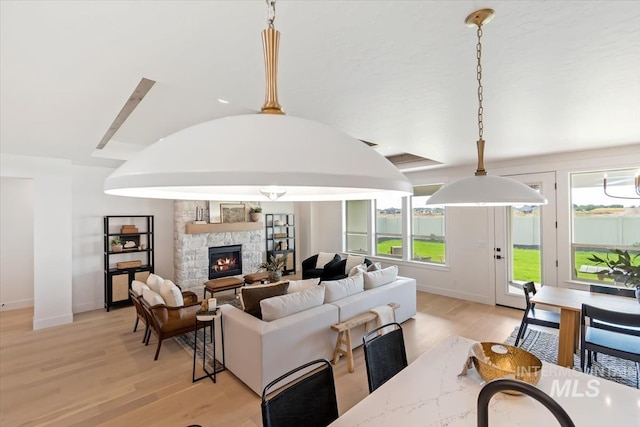 living area with lofted ceiling, plenty of natural light, light wood-style flooring, and a stone fireplace