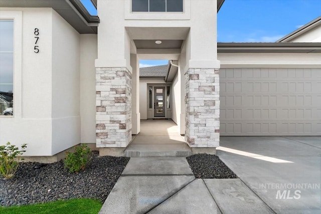 entrance to property with a garage, stone siding, concrete driveway, and stucco siding