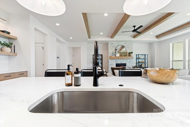 kitchen with a fireplace, a sink, open floor plan, beam ceiling, and light stone countertops