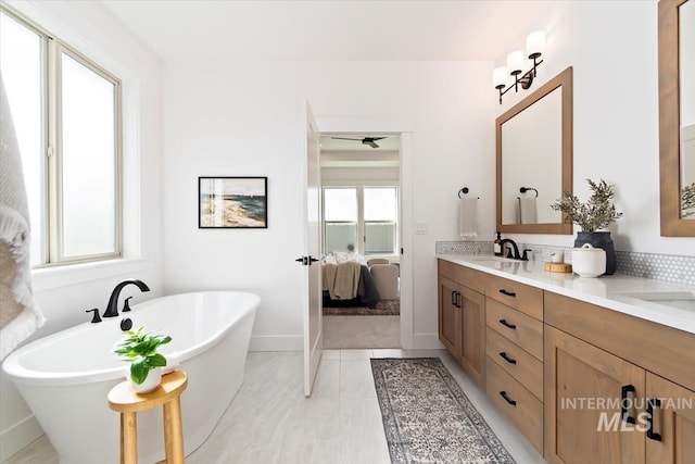 ensuite bathroom featuring a freestanding tub, connected bathroom, a sink, baseboards, and double vanity