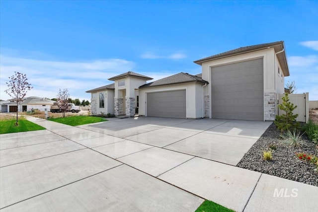 prairie-style house featuring concrete driveway, stone siding, an attached garage, and stucco siding