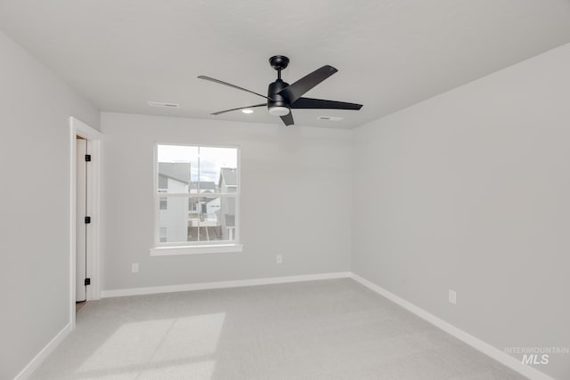 spare room featuring light colored carpet, visible vents, baseboards, and ceiling fan
