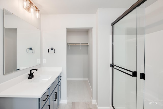full bath featuring vanity, baseboards, a stall shower, and a spacious closet