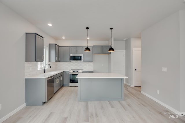 kitchen featuring gray cabinetry, a sink, backsplash, light wood-style floors, and stainless steel appliances
