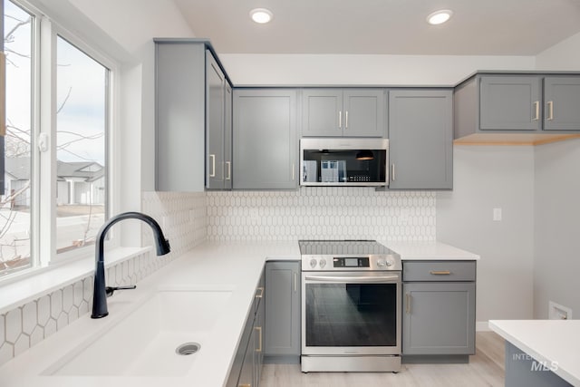 kitchen with a sink, light countertops, tasteful backsplash, appliances with stainless steel finishes, and gray cabinets