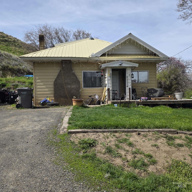 view of front of home featuring a chimney, metal roof, and a front yard