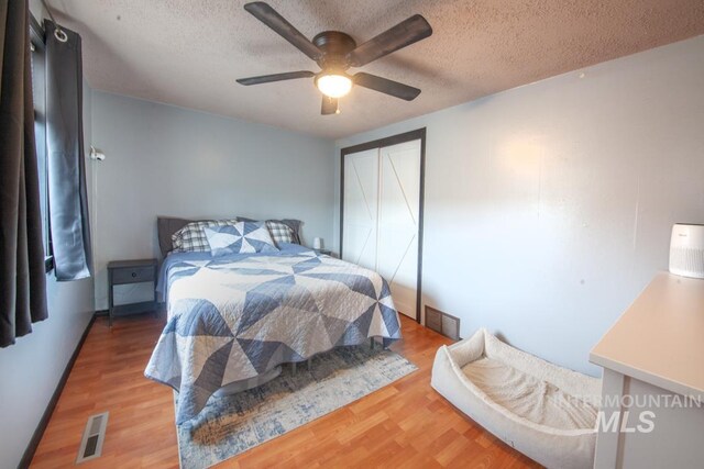 bedroom with a ceiling fan, wood finished floors, a textured ceiling, a closet, and visible vents