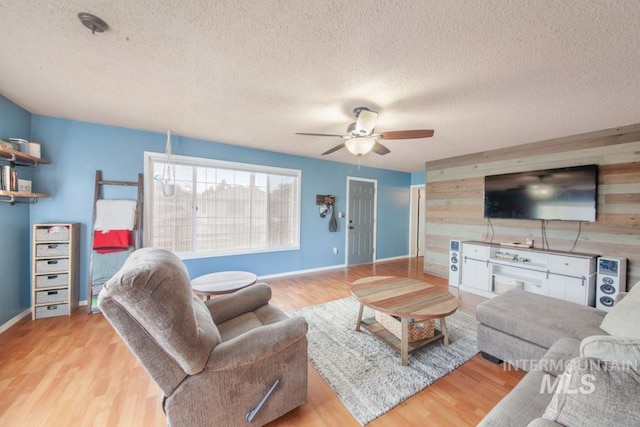 living room featuring wooden walls, light wood-type flooring, a textured ceiling, and a ceiling fan