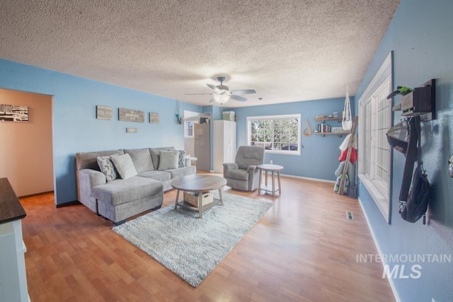 living area featuring ceiling fan, baseboards, wood finished floors, and a textured ceiling