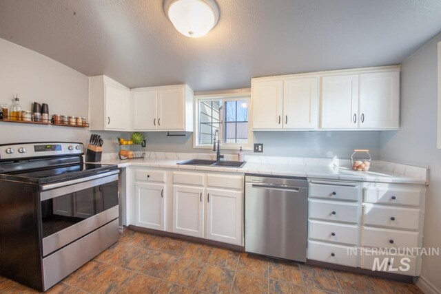 kitchen featuring stainless steel appliances, a sink, white cabinetry, stone finish flooring, and tile counters