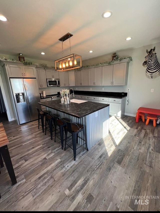 kitchen with gray cabinetry, a breakfast bar, stainless steel appliances, and dark wood finished floors