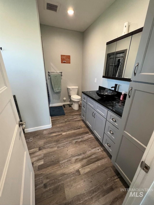 full bath featuring wood finished floors, toilet, vanity, baseboards, and visible vents