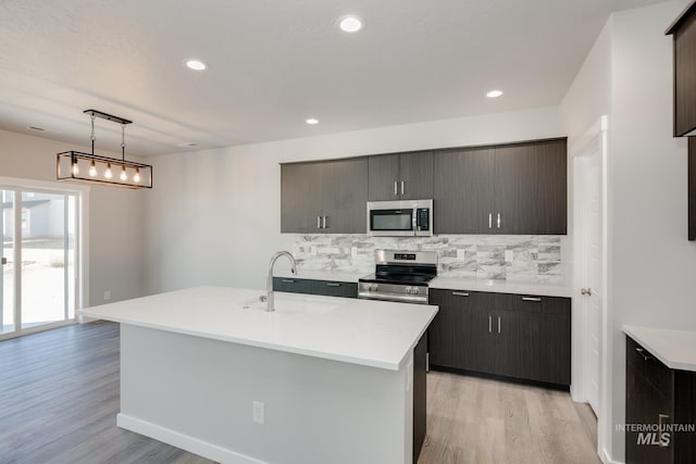 kitchen featuring a kitchen island with sink, hanging light fixtures, sink, appliances with stainless steel finishes, and light hardwood / wood-style floors