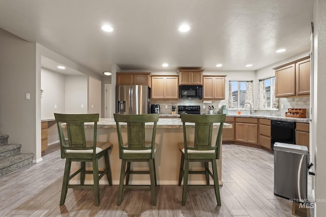 kitchen with light hardwood / wood-style floors, a kitchen island, a kitchen breakfast bar, and black appliances