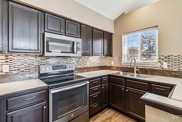 kitchen featuring appliances with stainless steel finishes, tasteful backsplash, sink, light hardwood / wood-style flooring, and dark brown cabinets