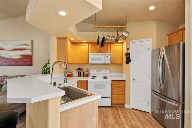 kitchen with light countertops, light wood-style floors, a sink, white appliances, and a peninsula