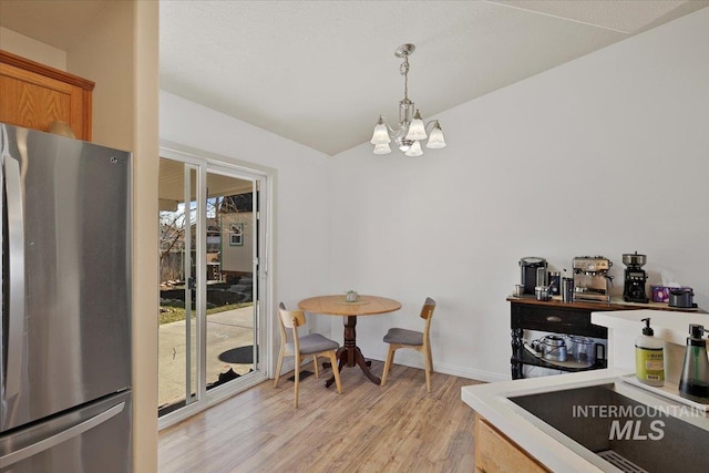 kitchen with pendant lighting, light wood finished floors, freestanding refrigerator, vaulted ceiling, and a chandelier